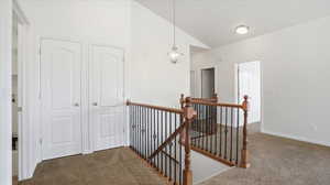 Hallway featuring an upstairs landing, vaulted ceiling, and dark carpet