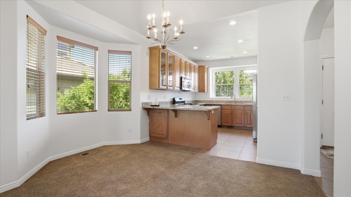 Kitchen and dining area featuring light wood cabinetry, stainless steel appliances, granite countertops, and tile flooring