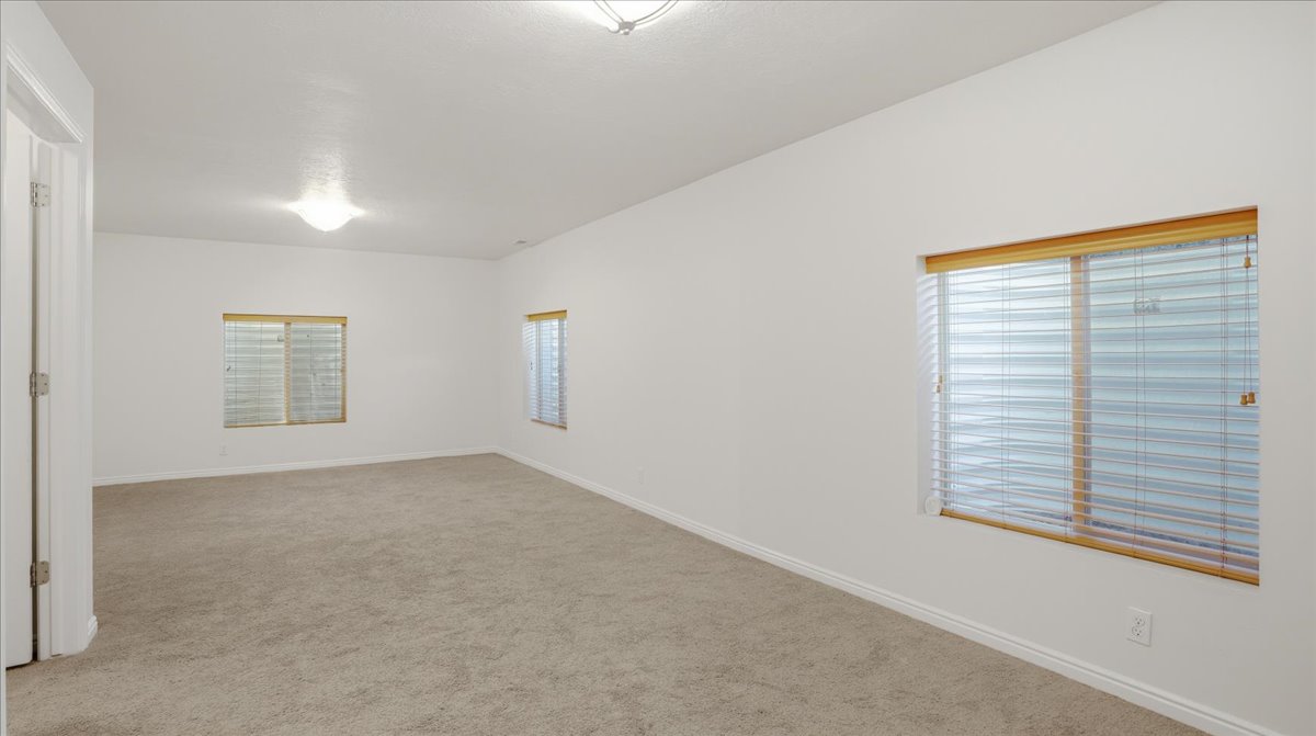 Carpeted room with white walls, multiple windows featuring blinds, and a flush mount ceiling light fixture