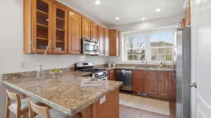 Kitchen with stainless steel appliances, a peninsula, wood finish cabinets, light stone countertops, and recessed lighting