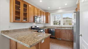 Kitchen featuring stainless steel appliances, a peninsula, wood finish cabinets, light stone counters, and recessed lighting