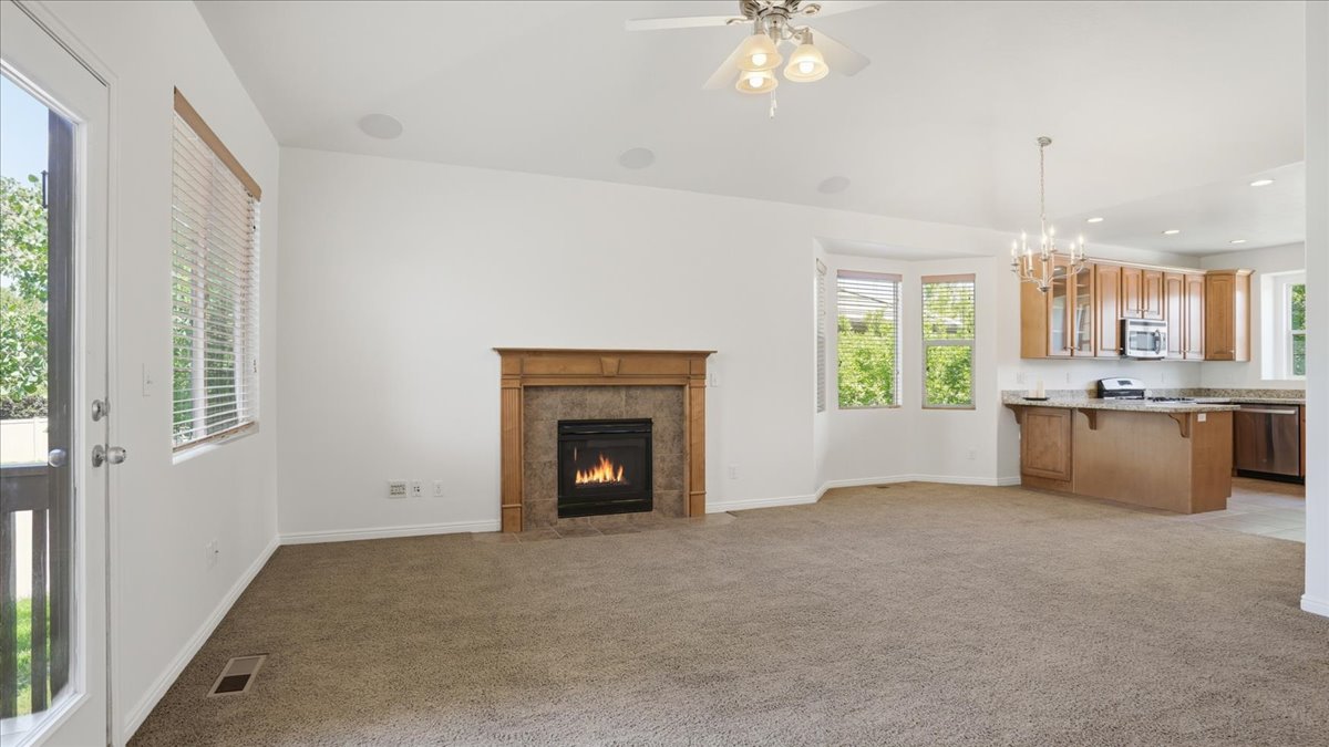 Spacious living area featuring a central fireplace with a wood mantle and tile surround, a ceiling fan with integrated lighting, and multiple windows providing natural light