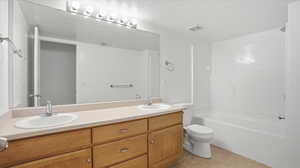 Full bath featuring double vanity, light tile patterned flooring, shower / bathtub combination, and a textured ceiling