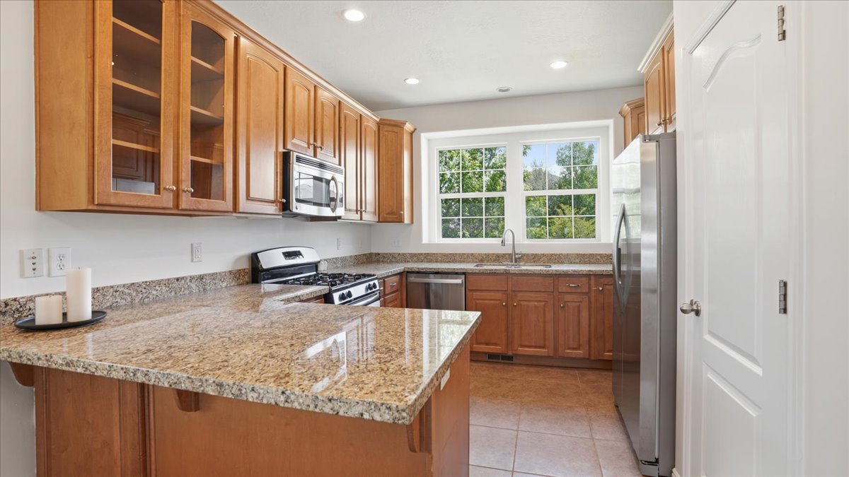 Modern kitchen featuring light wood cabinetry, stone countertops, stainless steel appliances, and recessed lighting