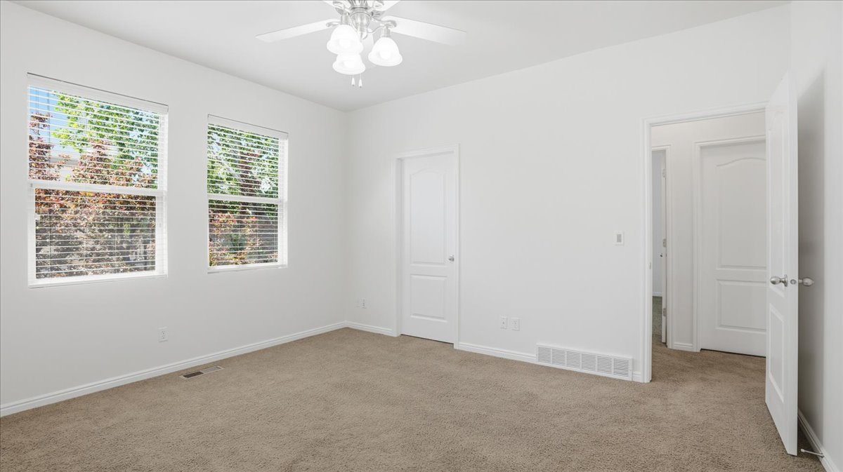 Carpeted interior space featuring two windows with horizontal blinds, a white ceiling fan with light fixture, and white painted walls