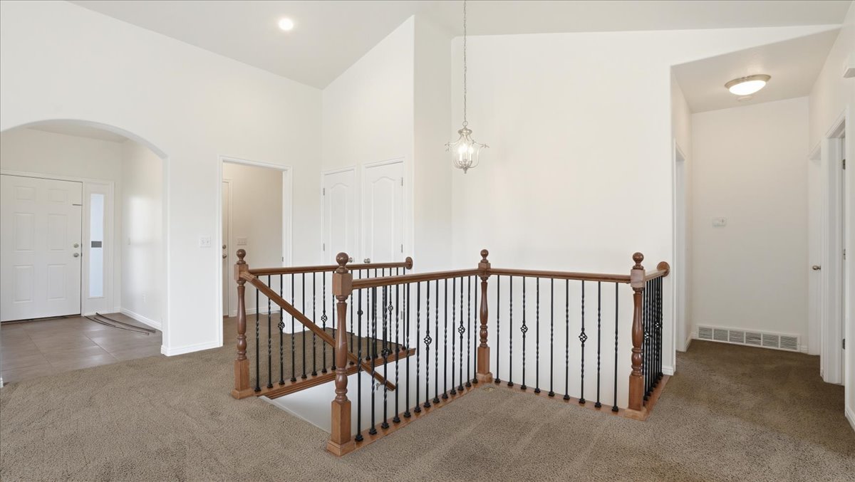 Hall featuring carpet, an upstairs landing, lofted ceiling, and arched walkways