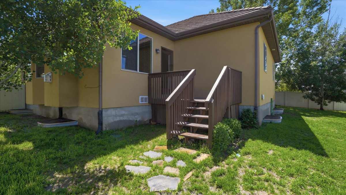 Rear exterior featuring a wood-toned deck with stairs, stucco siding, and a partial stone pathway