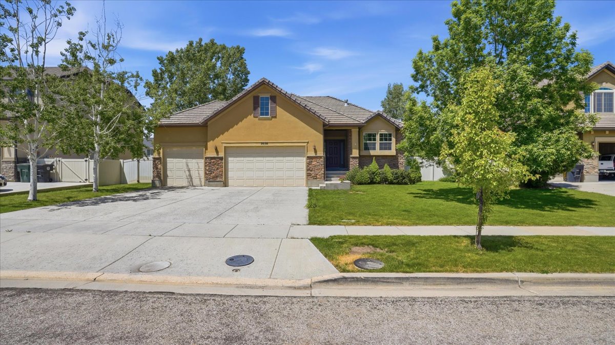 Exterior featuring a dual-tone stucco and stone facade, a multi-car driveway, an attached two-car garage, a covered front entry, and mature landscaping