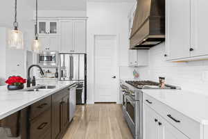 Dual tone kitchen with high end appliances, glass insert cabinets, hanging light fixtures, light wood-style floors, and light stone counters