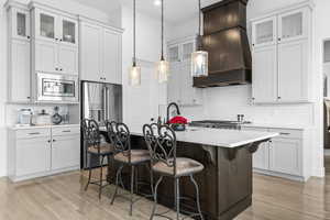 Kitchen with glass insert cabinets, dual tone cabinetry, stainless steel appliances, a kitchen bar, and a center island with sink