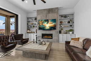 Living room with a tiled fireplace, a ceiling fan, and built in features