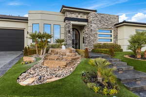 View of front of home with stone siding, stucco siding, an attached garage, and driveway