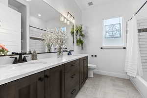 Bathroom with double vanity, shower / tub combo, and light stone finish floors