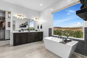 Bathroom featuring a walk in closet, double vanity, a soaking tub, light wood-style flooring, and a mountain view