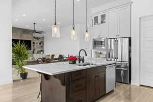 Kitchen featuring a breakfast bar area, glass insert cabinets, stainless steel appliances, light stone counters, and hanging light fixtures