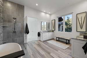 Full bath featuring walk in shower, two vanities, light wood-style floors, a freestanding tub, and recessed lighting