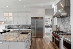 Kitchen with light stone countertops, white cabinets, built in appliances, decorative backsplash, and dark wood-type flooring