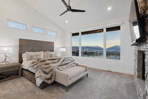 Bedroom with a stone fireplace, light carpet, a ceiling fan, and vaulted ceiling