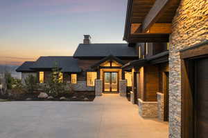 View of front facade featuring stone siding, french doors, a shingled roof, and a chimney