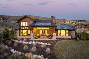 Back of house featuring a standing seam roof, stone siding, a patio, and a chimney