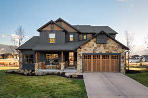 View of front of property with board and batten siding, a porch, a front lawn, stone siding, and driveway