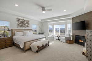 Bedroom featuring light colored carpet, a ceiling fan, a raised ceiling, a fireplace, and recessed lighting