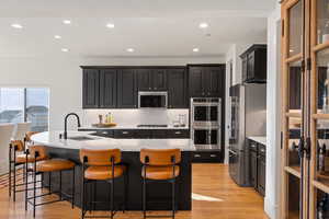 Kitchen featuring dark cabinetry, recessed lighting, a center island with sink, stainless steel appliances, and light wood-style floors