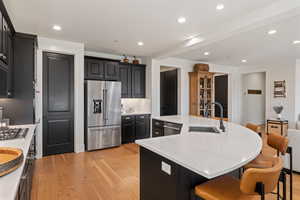 Kitchen with dark cabinets, a large island with sink, stainless steel appliances, and recessed lighting