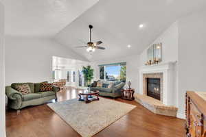 Living room featuring dark wood flooring, a ceiling fan, a fireplace, and a high ceiling