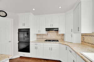 Kitchen with light stone counters, white cabinets, and recessed lighting