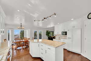 Kitchen featuring white cabinets, stainless steel appliances, light stone countertops, dark wood flooring, and a center island