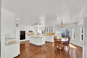 Kitchen with light stone counters, white cabinets, a chandelier, a center island, and tasteful backsplash