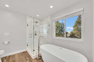 Remodeled Primary Bathroom with a shower stall, a freestanding bath, wood finished floors, and recessed lighting