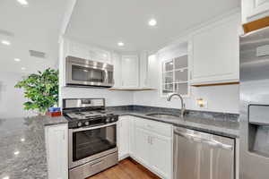 Basement Kitchen featuring stainless steel appliances, white cabinetry, dark stone countertops, light wood finished floors, and recessed lighting