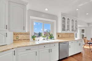 Kitchen with light stone counters, stainless steel dishwasher, white cabinets, glass insert cabinets, and recessed lighting