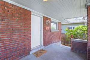 View of exterior entry featuring covered porch and brick siding