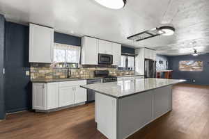 Kitchen featuring a center island, dark stone countertops, white cabinetry, stainless steel appliances, and dark wood-style flooring