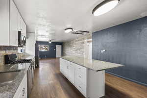 Kitchen featuring white cabinetry, dark stone countertops, dark wood-style flooring, a kitchen island, and stainless steel appliances