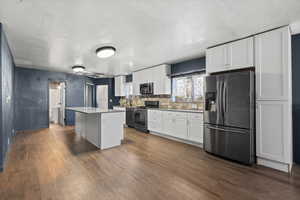 Kitchen featuring stainless steel appliances, white cabinets, dark wood-type flooring, a kitchen island, and decorative backsplash