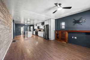 Kitchen featuring white cabinetry, stainless steel appliances, dark wood-style flooring, a kitchen island, and open floor plan