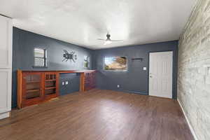 Unfurnished living room with a ceiling fan, dark wood-style floors, an accent wall, and a textured ceiling