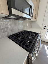 Kitchen view of stainless steel appliances, light stone counters, tasteful backsplash, light wood finish cabinets, and light wood-style flooring