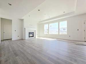 Unfurnished living room featuring light wood-type flooring, a tray ceiling, a glass covered fireplace, and recessed lighting
