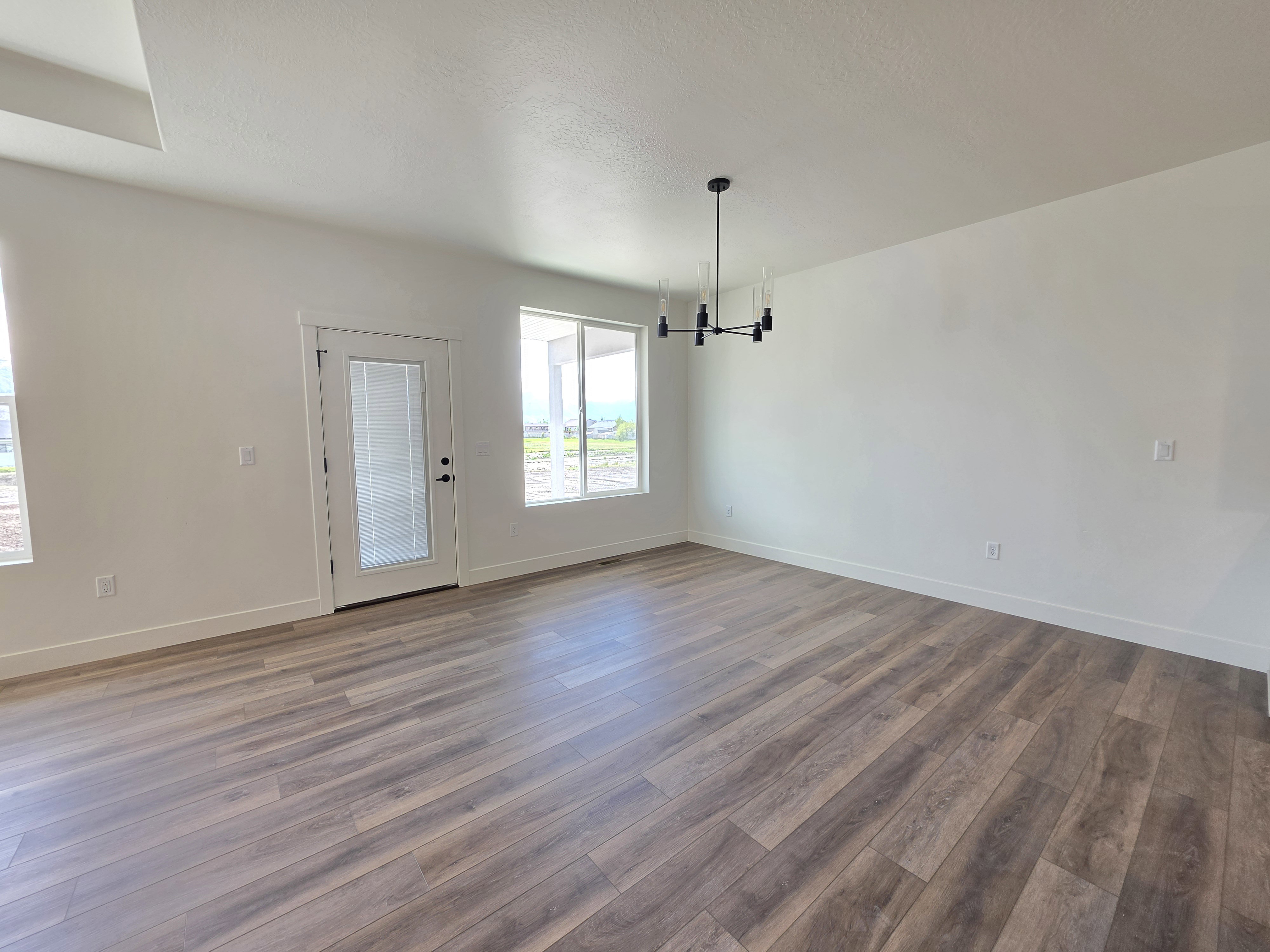 Expansive room featuring wood-finish flooring, white walls, and a contemporary chandelier