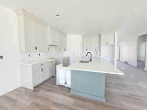 Kitchen with a kitchen island with sink, light wood finished floors, and decorative backsplash