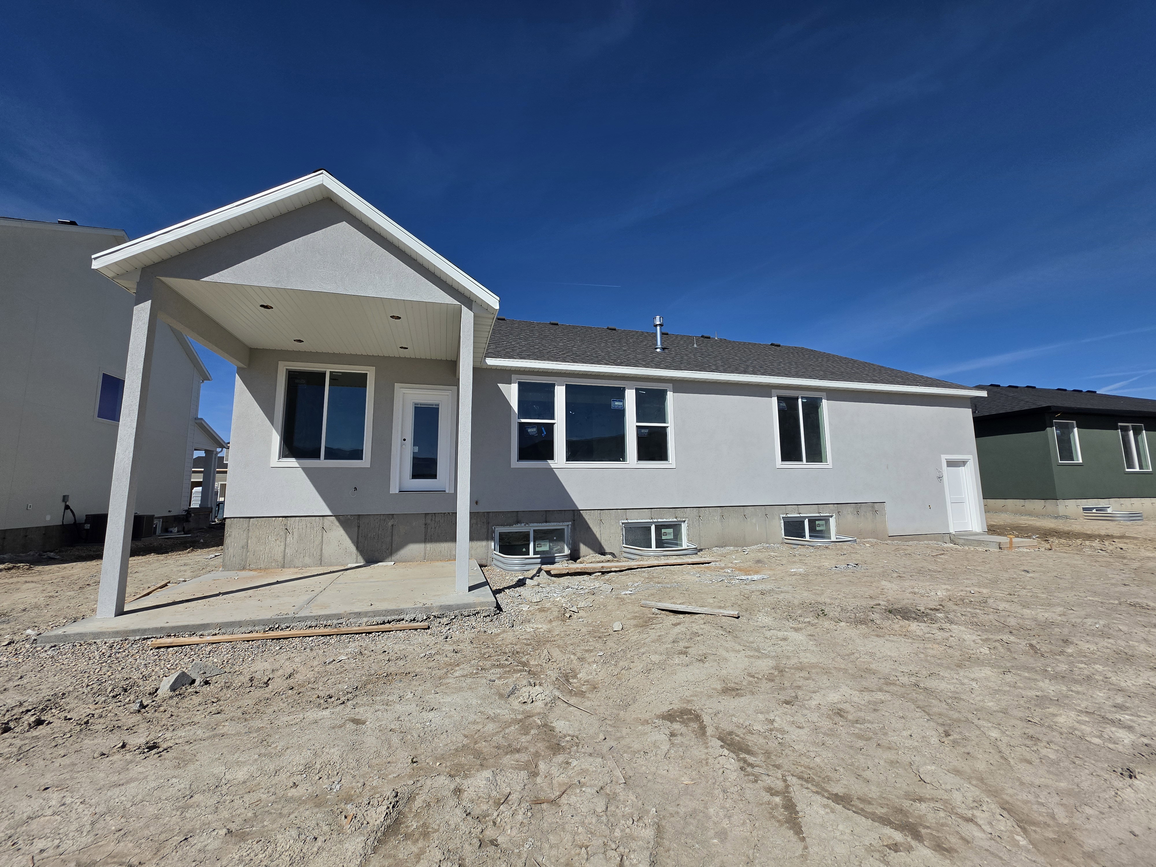 Contemporary stucco exterior featuring a covered patio, multiple windows, a rear entry door, and a basement access door