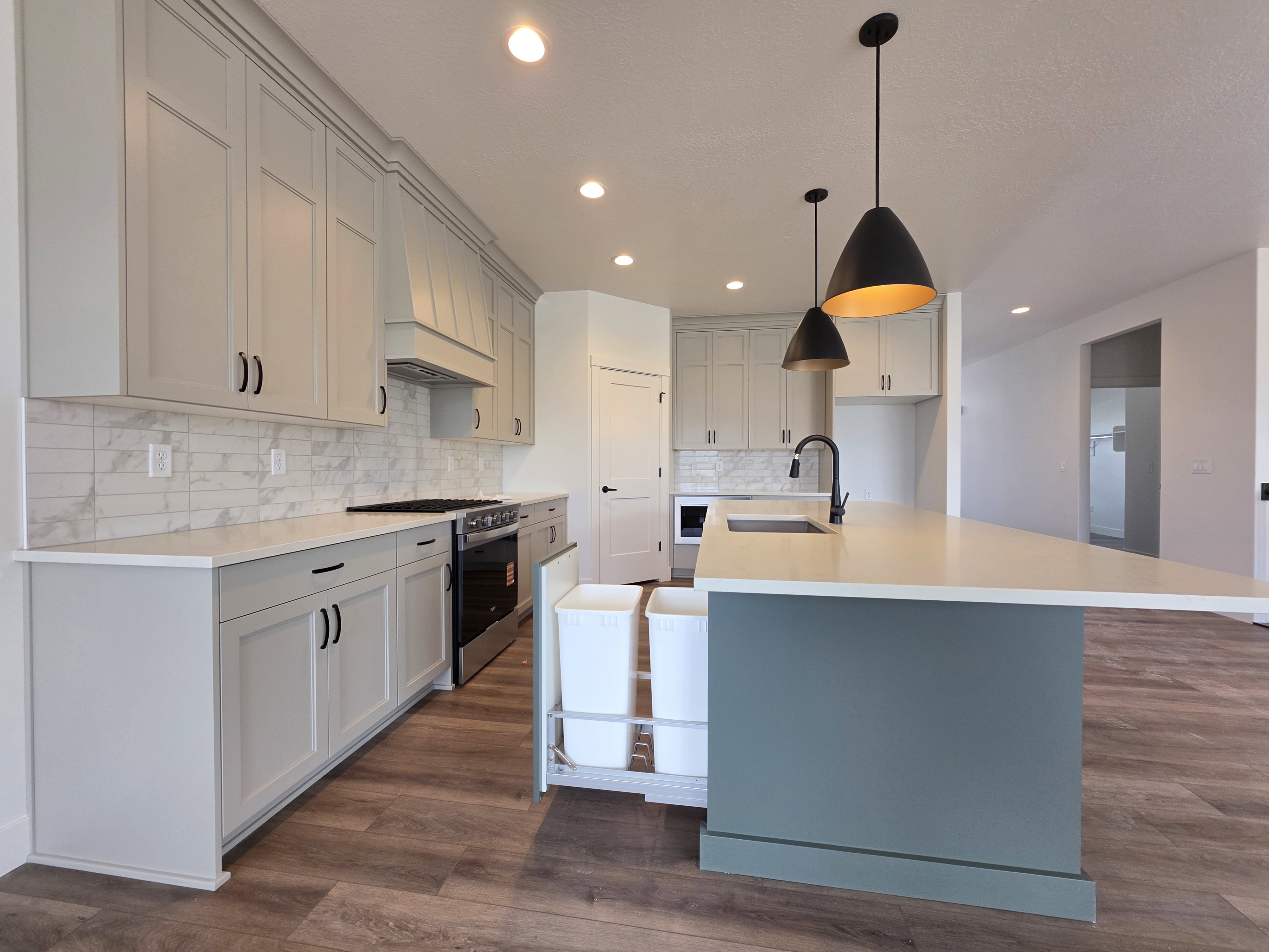Modern kitchen featuring light gray shaker cabinetry, wood-finish flooring, a white subway tile backsplash, and recessed lighting