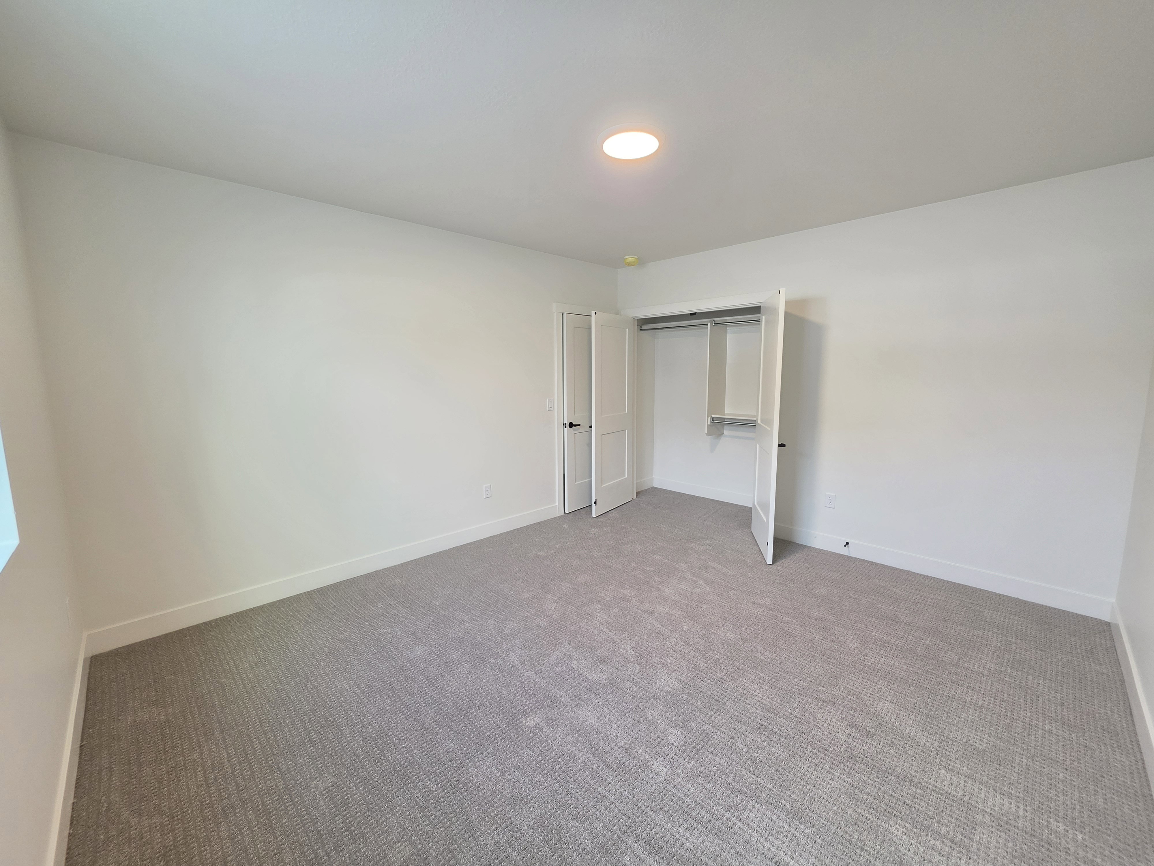 Spacious room featuring neutral carpeting, white walls, and a ceiling-mounted light fixture