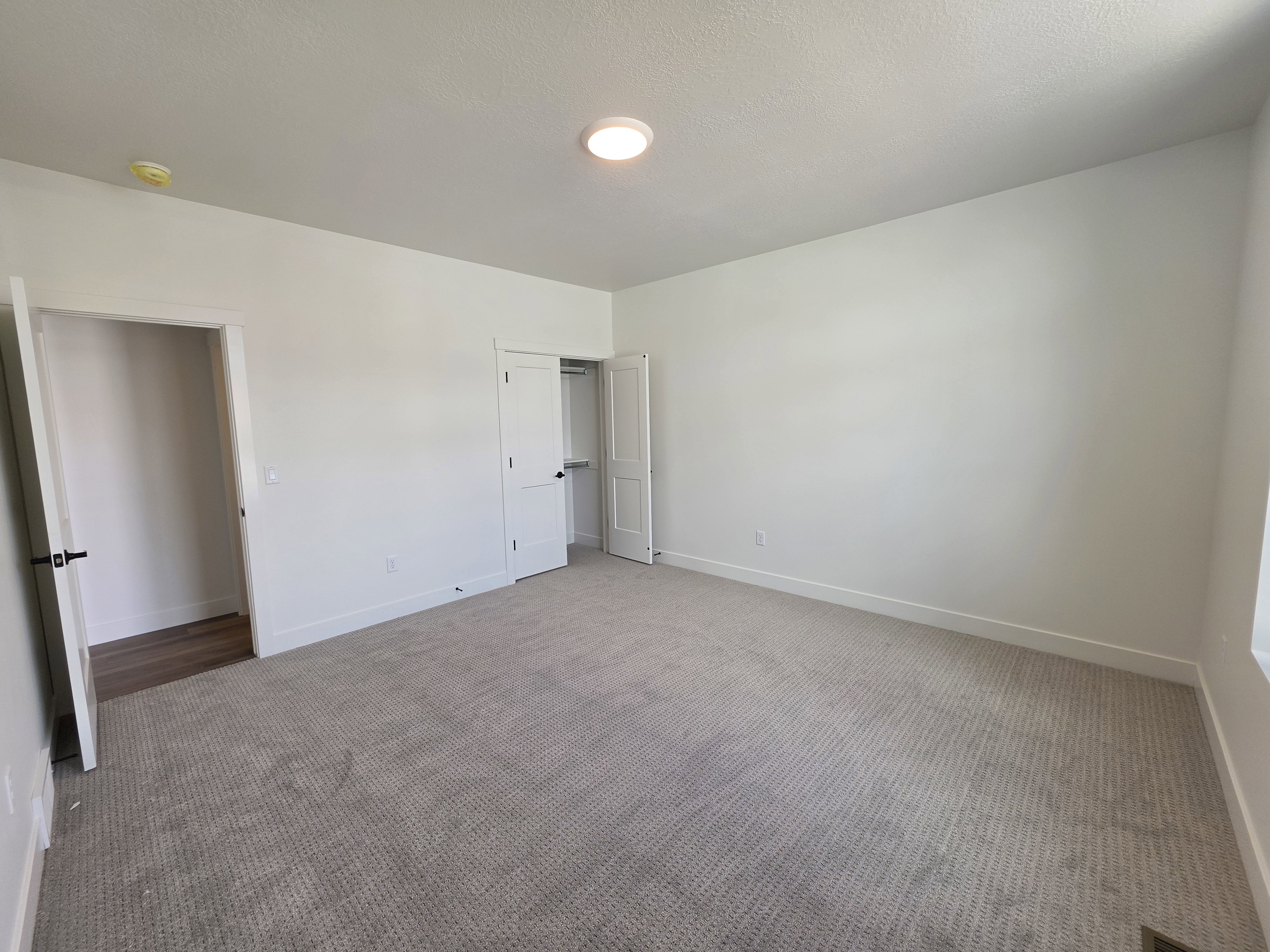 Spacious room featuring neutral carpeting, white walls, and a modern ceiling light fixture