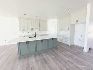 Kitchen featuring two tone color scheme, a kitchen island with sink, light wood finished floors, decorative backsplash, and light stone countertops